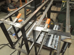 Welded anti-rattle ratchet strap tabs to under subframe storage box mounts